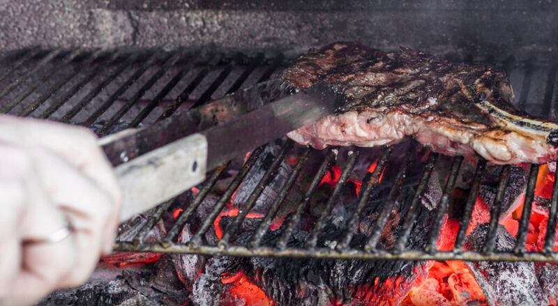 Mano humana asar carne en la parrilla de la barbacoa